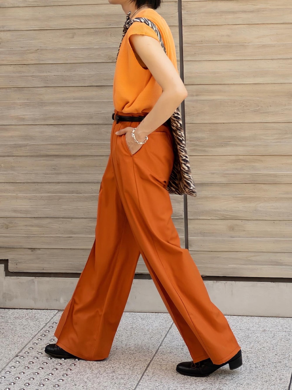 オレンジ系のTシャツ/カットソー、オレンジ系のスラックス、ブラック系のブーツを着用したメンズの夏コーディネートの4枚目の写真