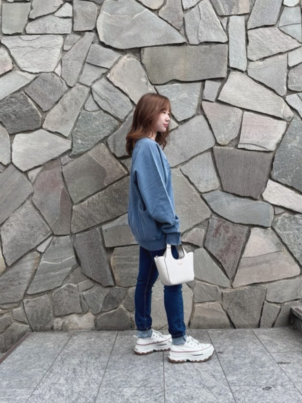 ブルー系のデニムパンツ、ホワイト系のショルダーバッグ、ブルー系のスウェットを着用したレディースの秋コーディネートの3枚目の写真