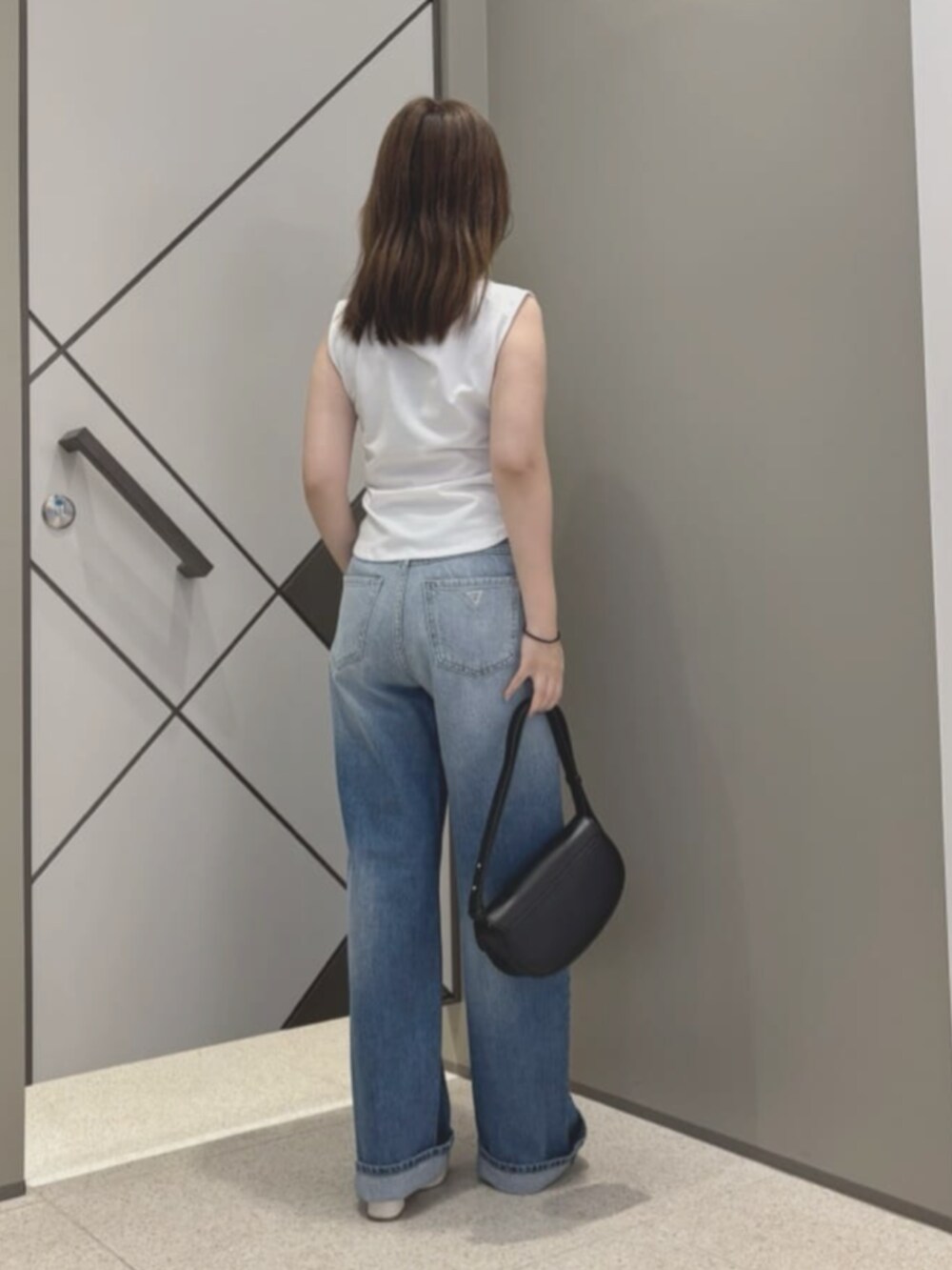 ブルー系のデニムパンツ、ホワイト系のタンクトップ、ブラック系のハンドバッグを着用したレディースの夏コーディネートの2枚目の写真