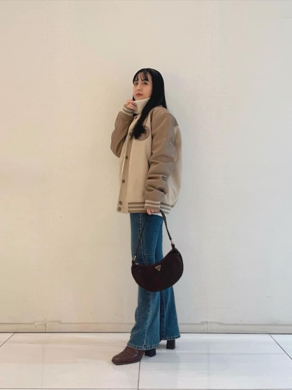 ブルー系のデニムパンツ、ブラウン系のショルダーバッグ、ベージュ系のスタジャンを着用したレディースの秋コーディネートの3枚目の写真