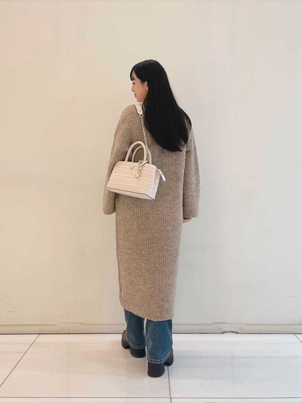 ブルー系のデニムパンツ、ホワイト系のニット/セーター、ホワイト系のショルダーバッグを着用したレディースの秋コーディネートの2枚目の写真