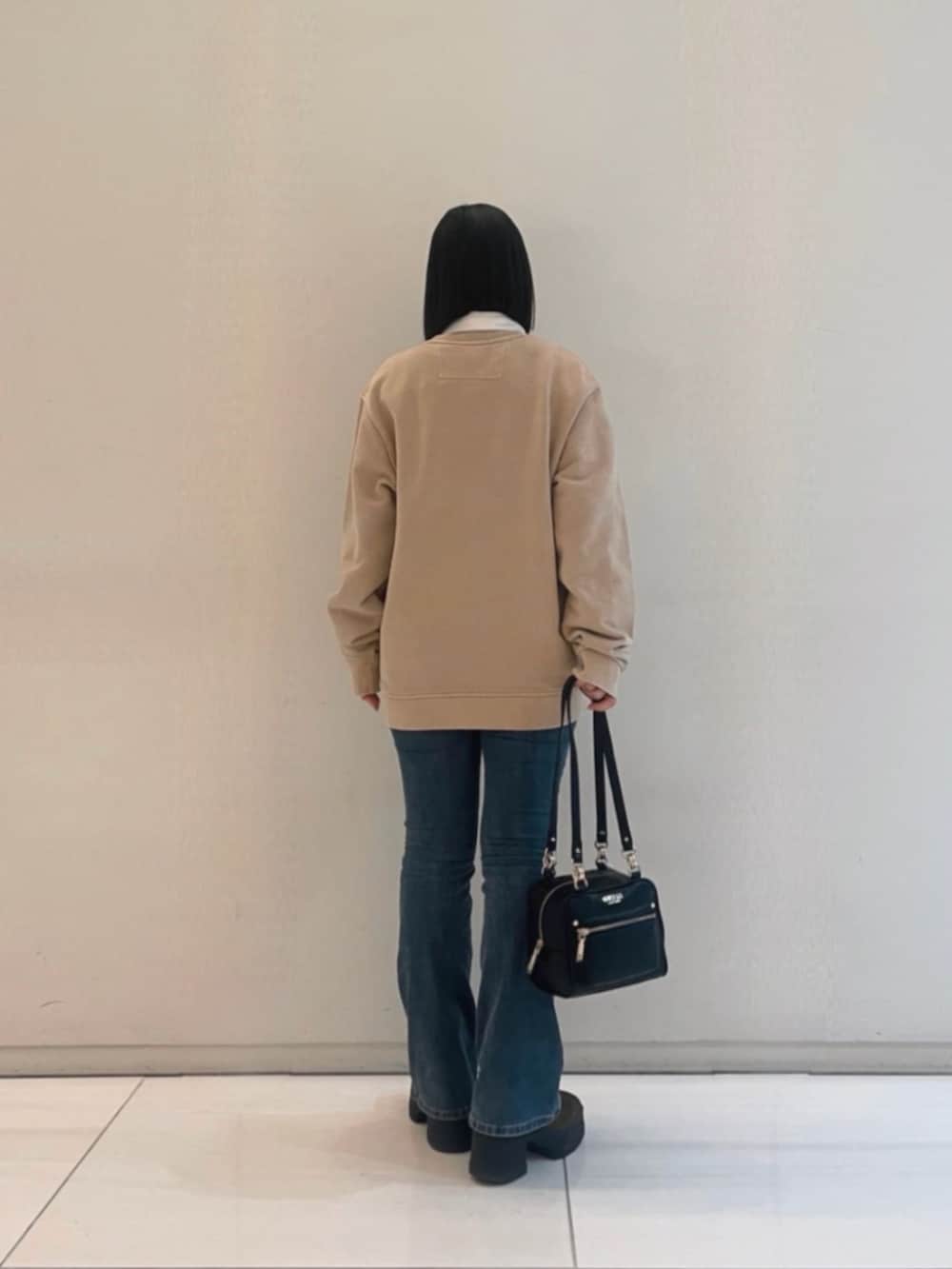 ブルー系のデニムパンツ、ベージュ系のポロシャツ、ブラック系のショルダーバッグを着用したレディースの冬コーディネートの2枚目の写真