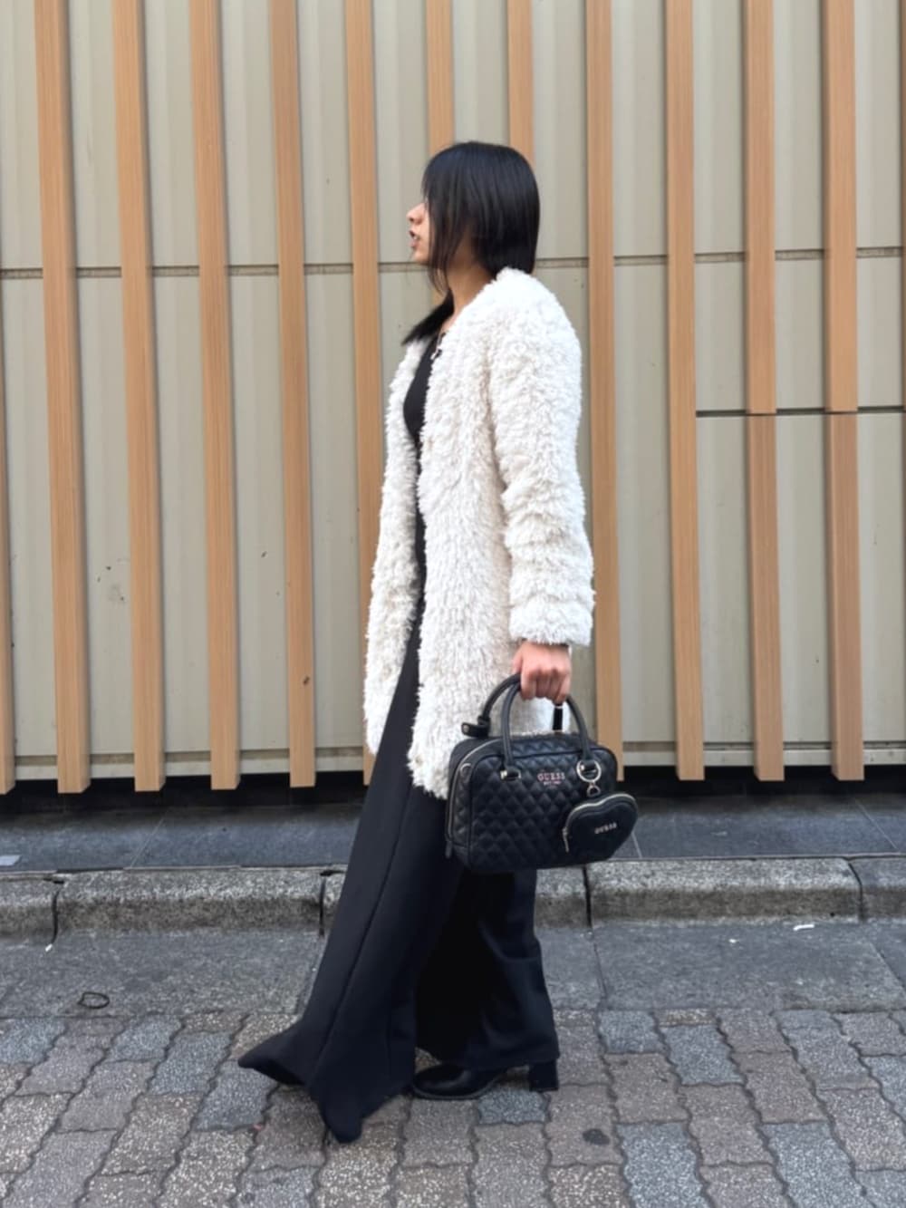 ブラック系のハンドバッグ、ブラック系のワンピース、ホワイト系のカーディガン/ボレロを着用したレディースの春コーディネートの5枚目の写真