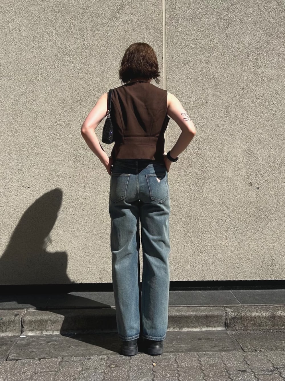 ブラウン系のベスト、ブルー系のデニムパンツ、ブラック系のハンドバッグを着用したレディースの夏コーディネートの2枚目の写真