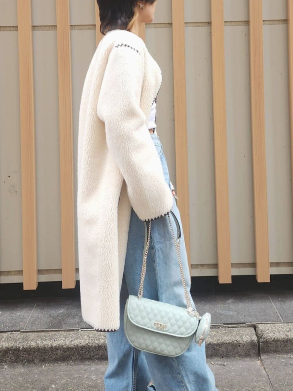 ホワイト系のタンクトップ、ブルー系のデニムパンツ、ホワイト系のノーカラージャケットを着用したレディースの冬コーディネートの4枚目の写真