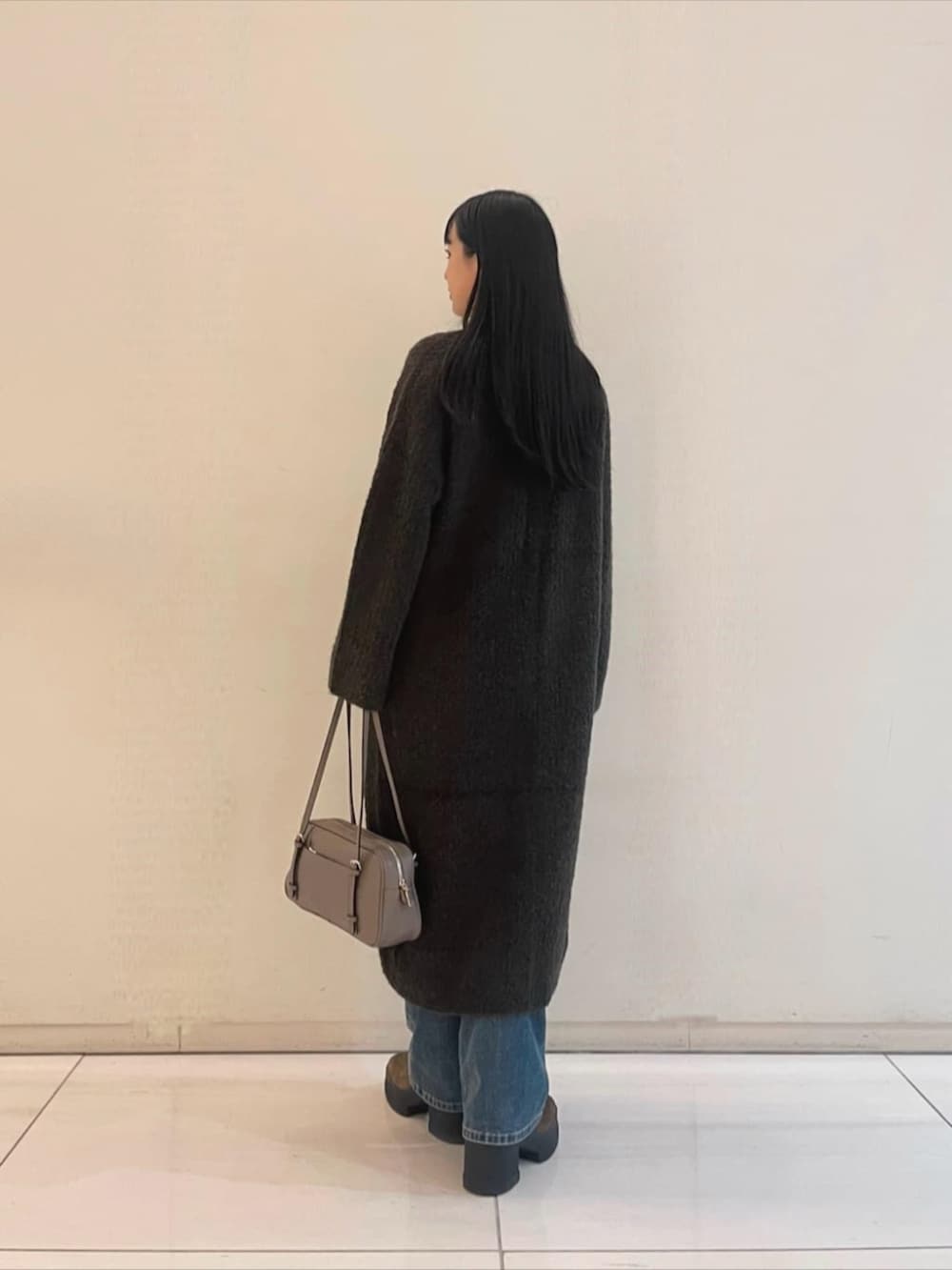 ブルー系のデニムパンツ、ホワイト系のニット/セーター、ベージュ系のショルダーバッグを着用したレディースの秋コーディネートの2枚目の写真