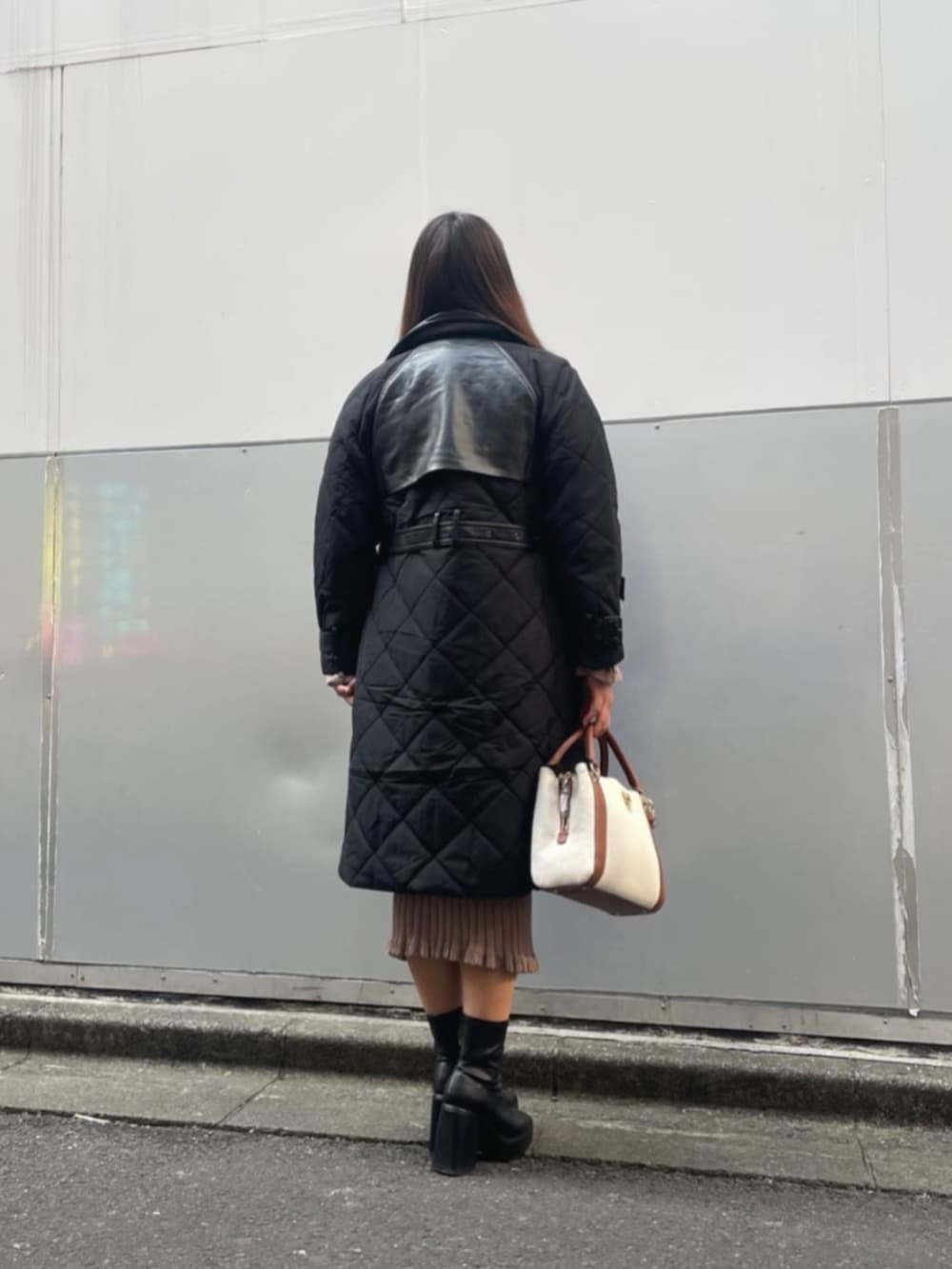 ブラック系のトレンチコート、ベージュ系のワンピース、イエロー系のハンドバッグを着用したレディースの冬コーディネートの2枚目の写真