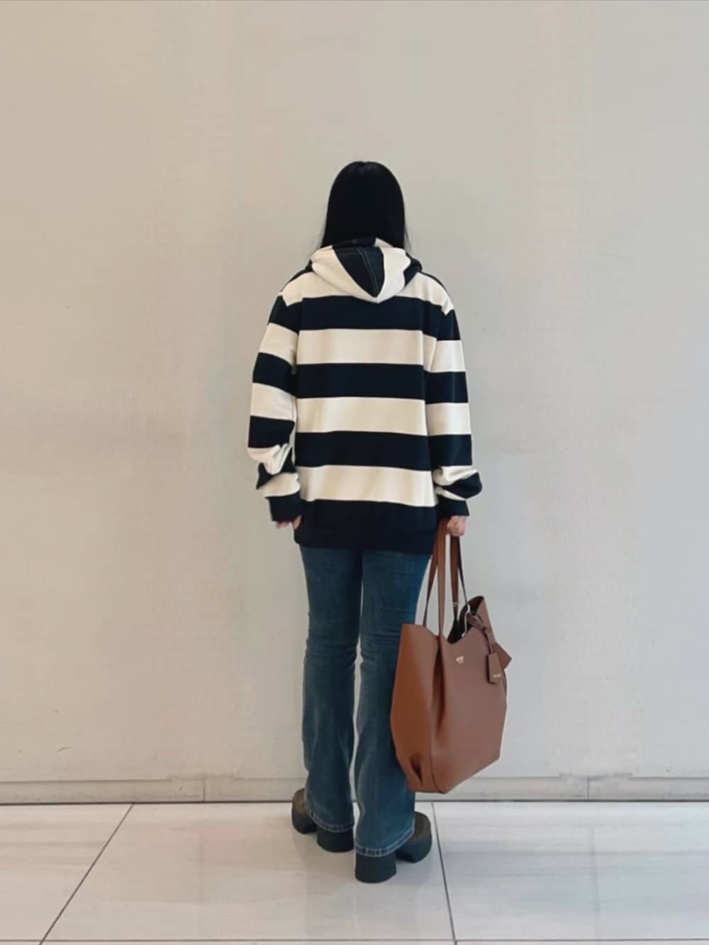 ブルー系のデニムパンツ、ブラウン系のトートバッグ、ブルー系のパーカーを着用したレディースの秋コーディネートの2枚目の写真