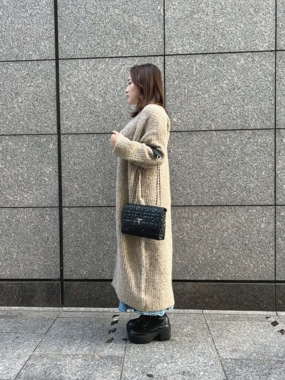 ブラック系のショルダーバッグ、ブルー系のデニムスカート、ホワイト系のニット/セーターを着用したレディースの秋コーディネートの3枚目の写真