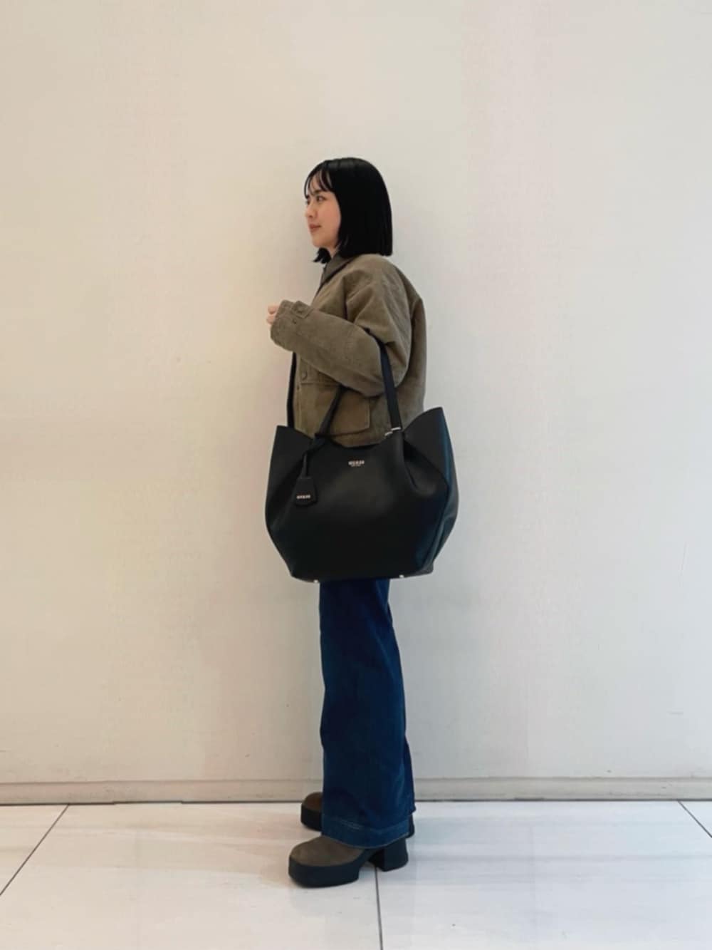 ブルー系のデニムパンツ、ブラック系のトートバッグ、グリーン系のミリタリージャケットを着用したレディースの冬コーディネートの3枚目の写真