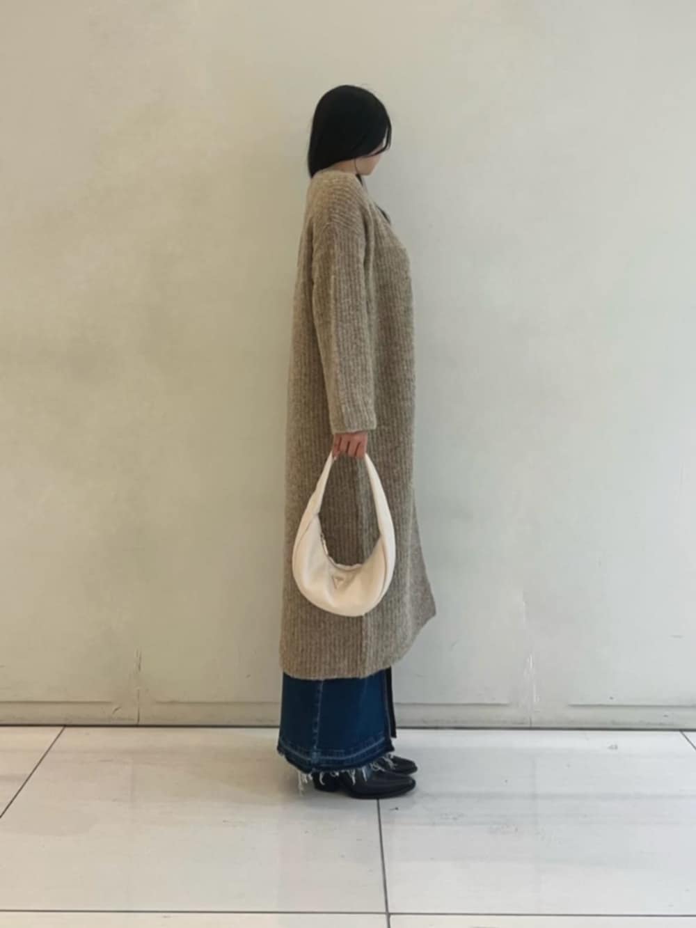 ブルー系のデニムスカート、ホワイト系のニット/セーター、ベージュ系のカーディガン/ボレロを着用したレディースの秋コーディネートの3枚目の写真