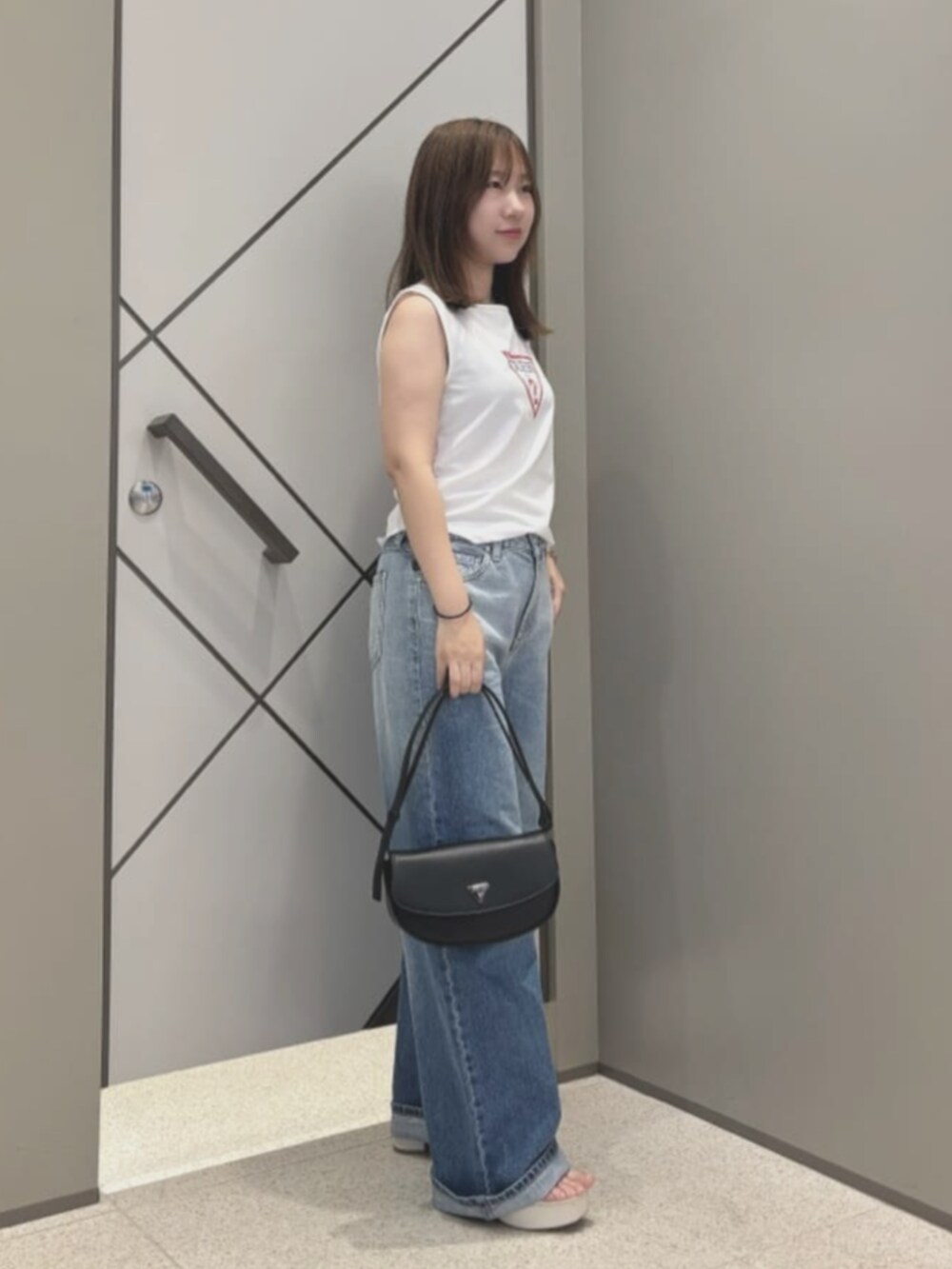 ブルー系のデニムパンツ、ホワイト系のタンクトップ、ブラック系のハンドバッグを着用したレディースの夏コーディネートの3枚目の写真