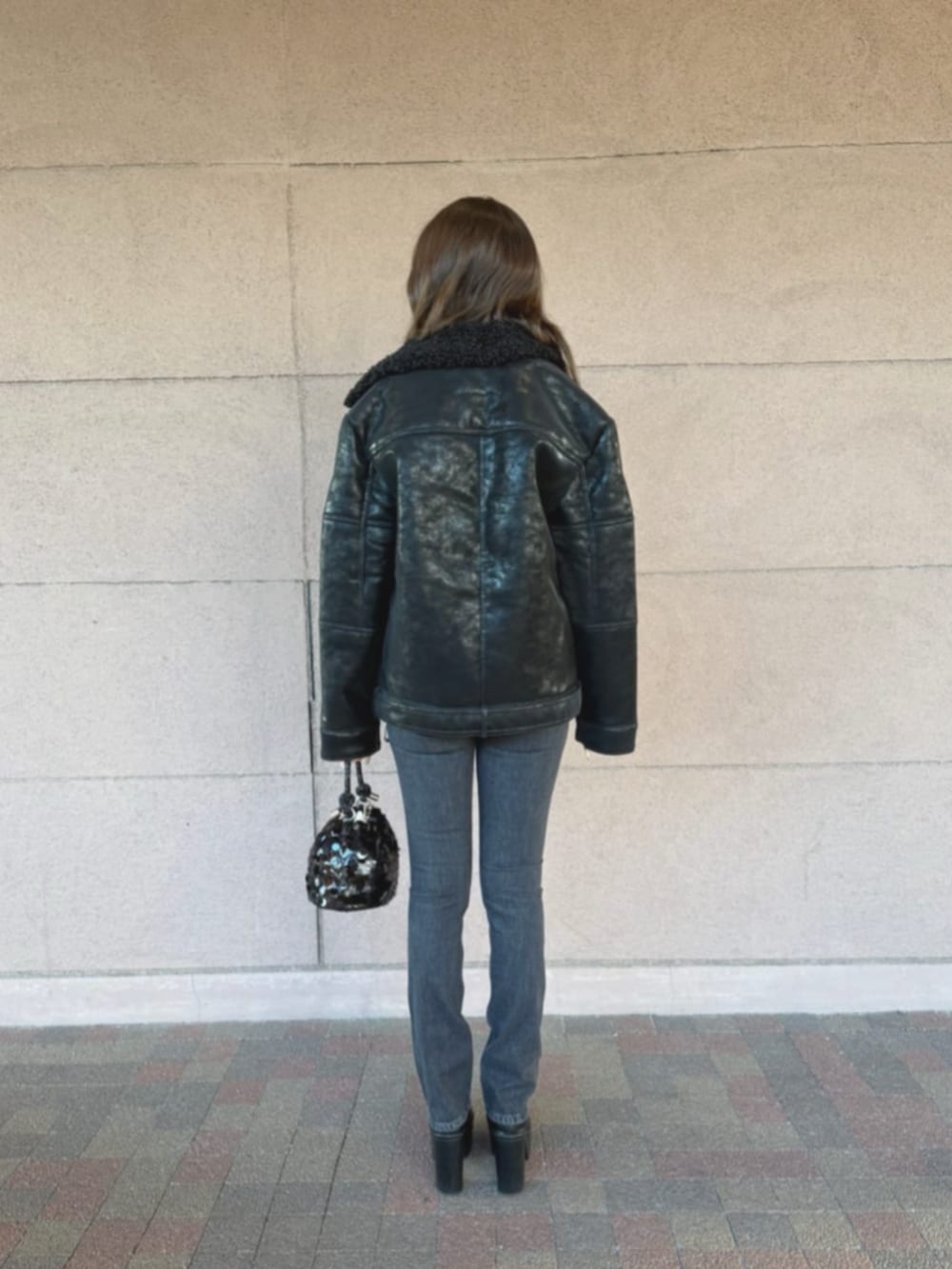 ブラック系のライダースジャケット、ブラック系のショルダーバッグ、ブラック系のデニムパンツを着用したレディースの冬コーディネートの2枚目の写真