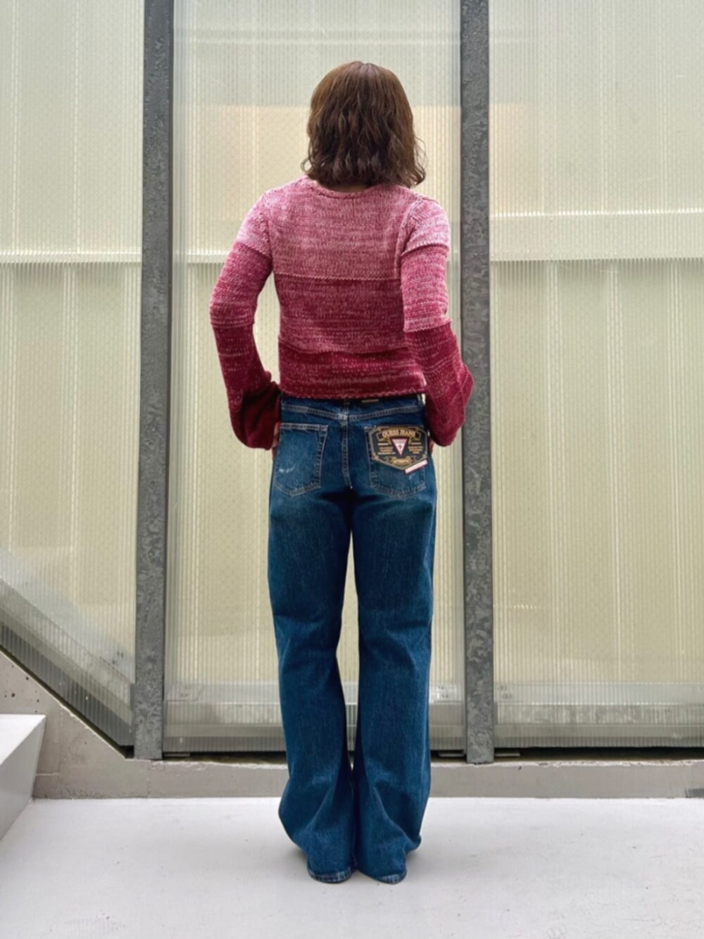 レッド系のニット/セーター、ブルー系のデニムパンツを着用したレディースの秋コーディネートの2枚目の写真