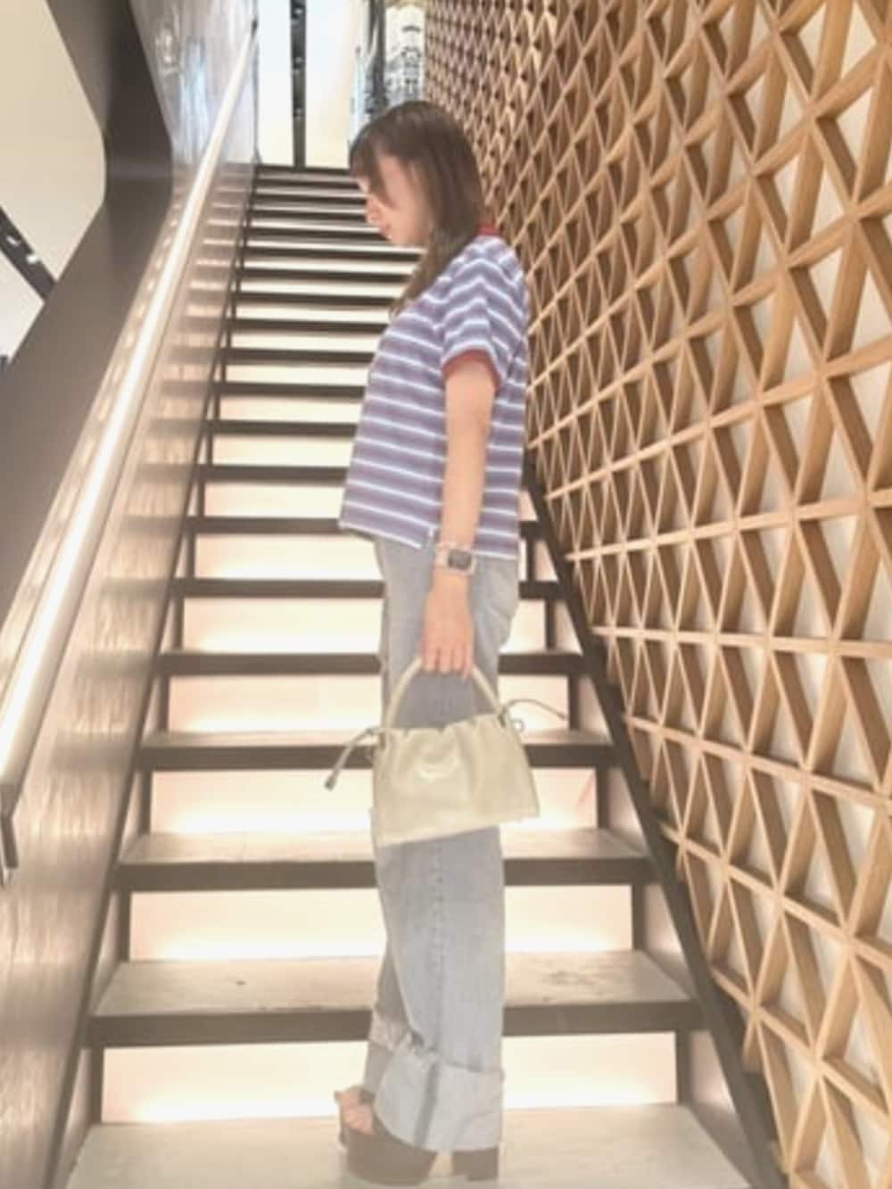 ブルー系のデニムパンツ、ブルー系のポロシャツ、ベージュ系のショルダーバッグを着用したレディースの夏コーディネートの3枚目の写真