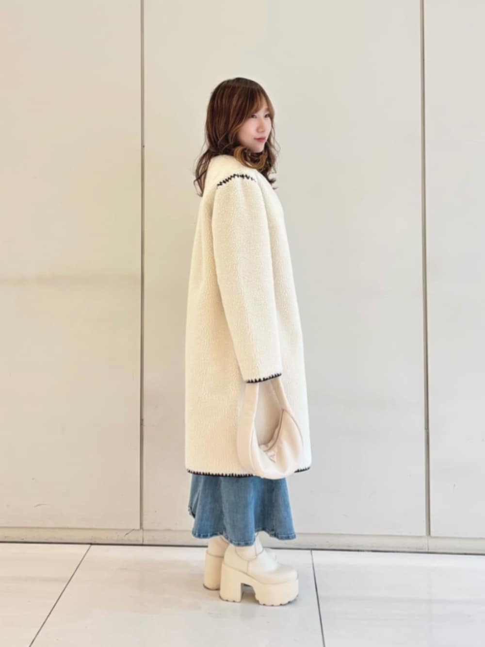 ブラック系のニット/セーター、ブルー系のデニムスカート、ホワイト系のショルダーバッグを着用したレディースの冬コーディネートの3枚目の写真