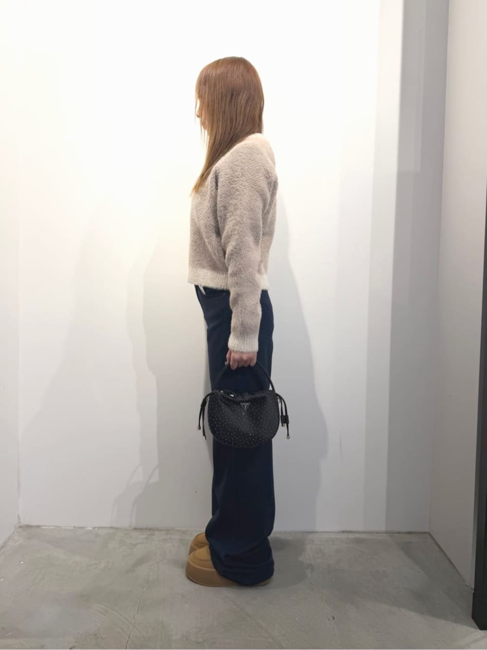 ブルー系のデニムパンツ、ベージュ系のニット/セーター、ブラック系のハンドバッグを着用したレディースの春コーディネートの3枚目の写真