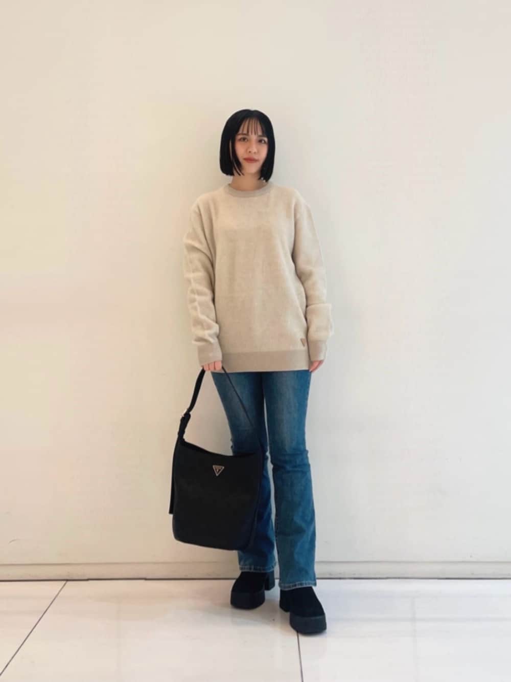 ブルー系のデニムパンツ、ベージュ系のニット/セーター、ブラック系のハンドバッグを着用したレディースの冬コーディネートの4枚目の写真