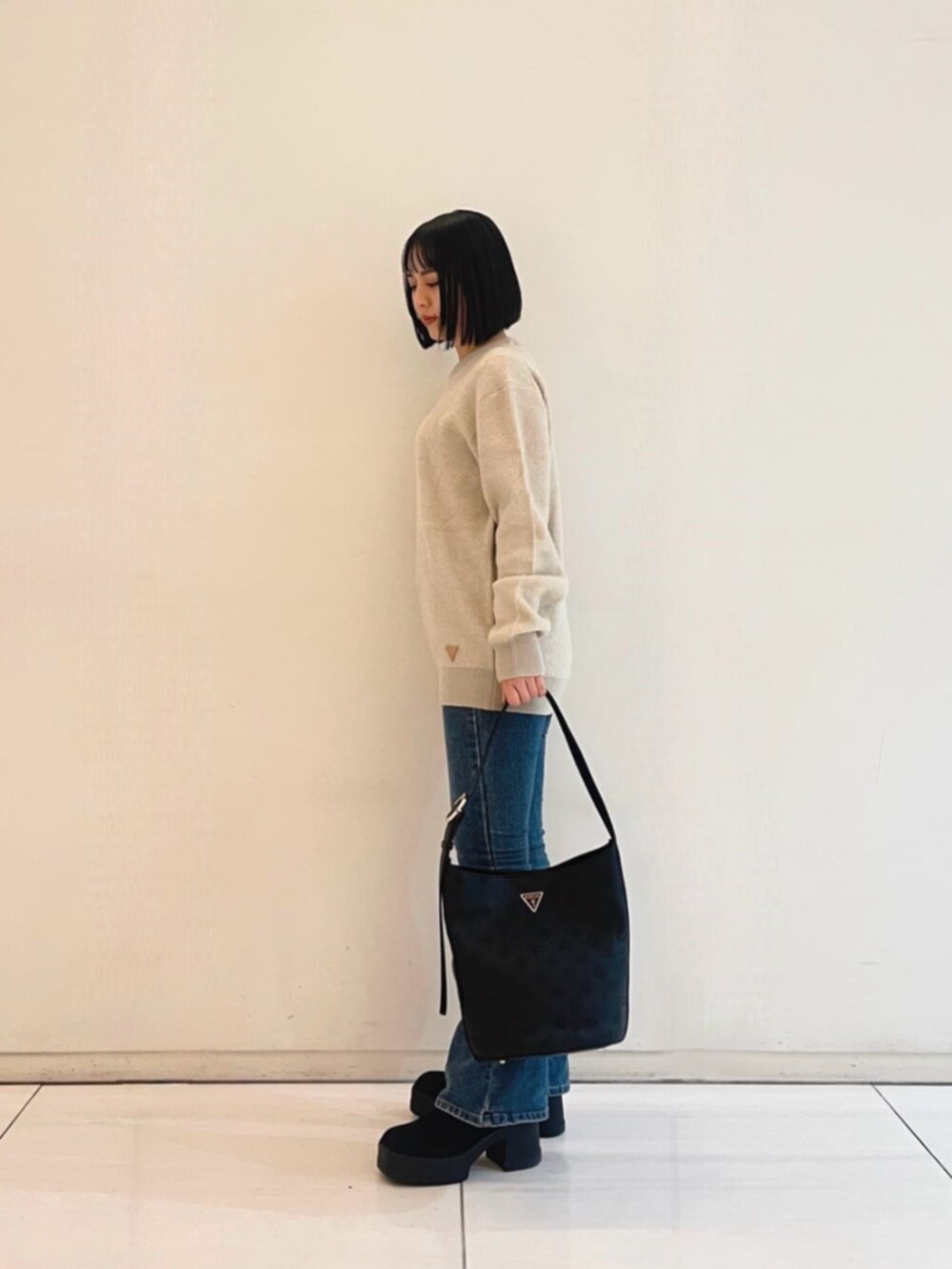 ブルー系のデニムパンツ、ベージュ系のニット/セーター、ブラック系のハンドバッグを着用したレディースの冬コーディネートの3枚目の写真