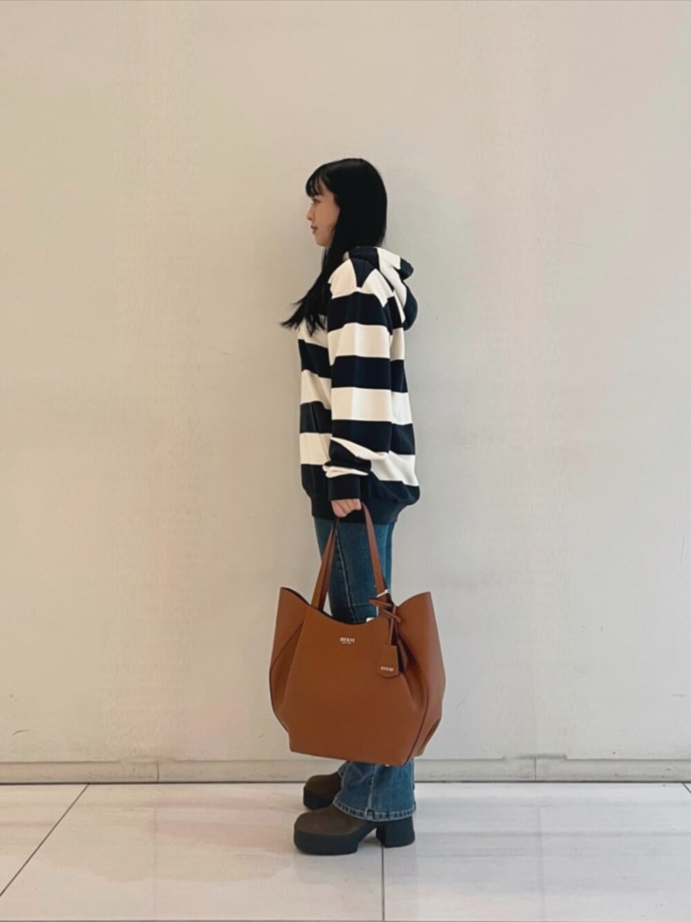 ブルー系のデニムパンツ、ブラウン系のトートバッグ、ブルー系のパーカーを着用したレディースの秋コーディネートの3枚目の写真