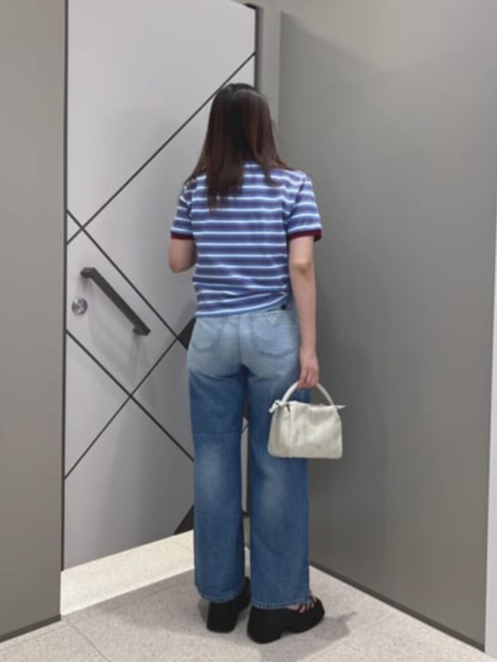 ブルー系のポロシャツ、ベージュ系のショルダーバッグ、ブルー系のデニムパンツを着用したレディースの夏コーディネートの2枚目の写真