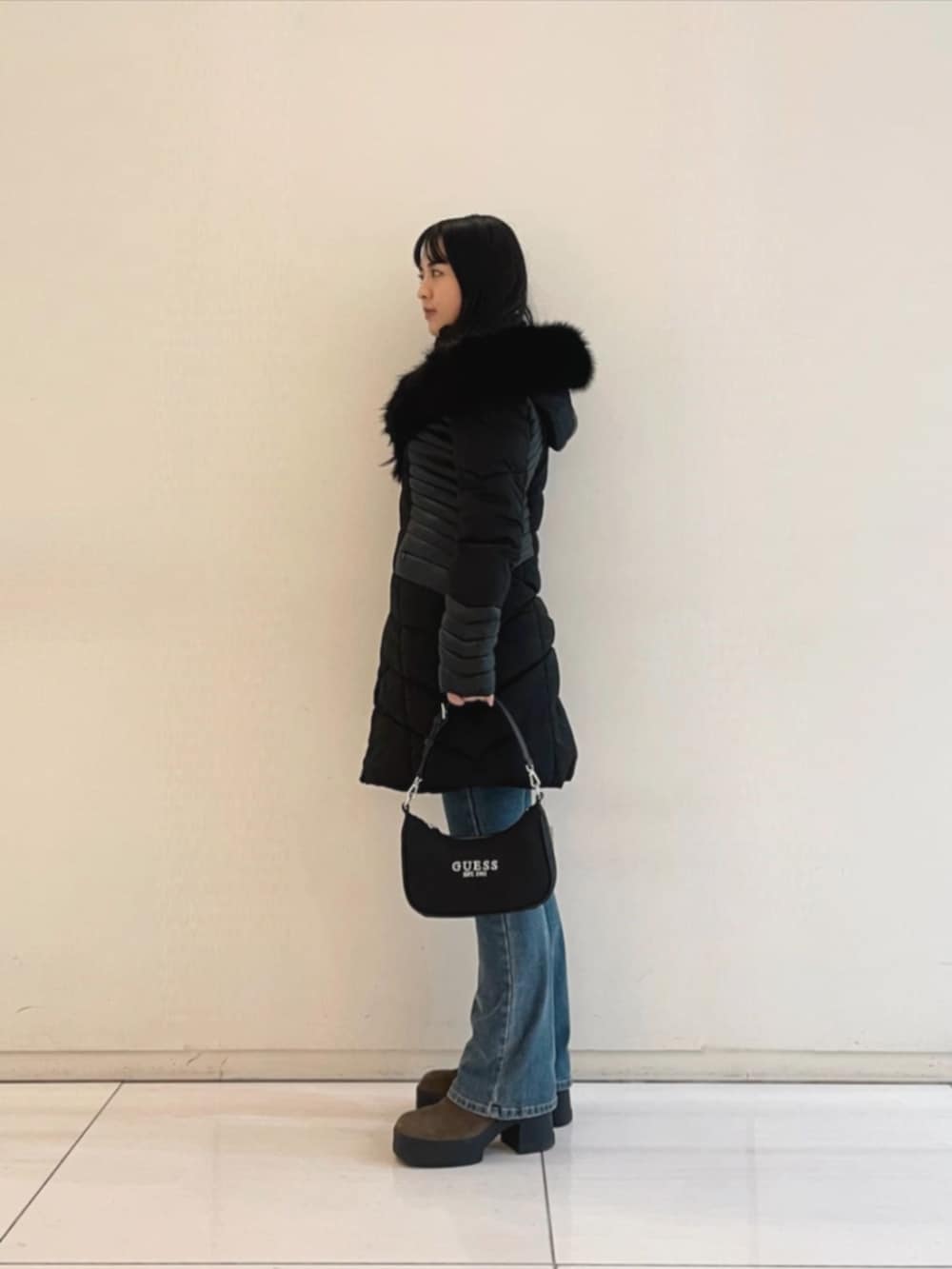 ブルー系のデニムパンツ、ホワイト系のニット/セーター、ブラック系のショルダーバッグを着用したレディースの冬コーディネートの3枚目の写真