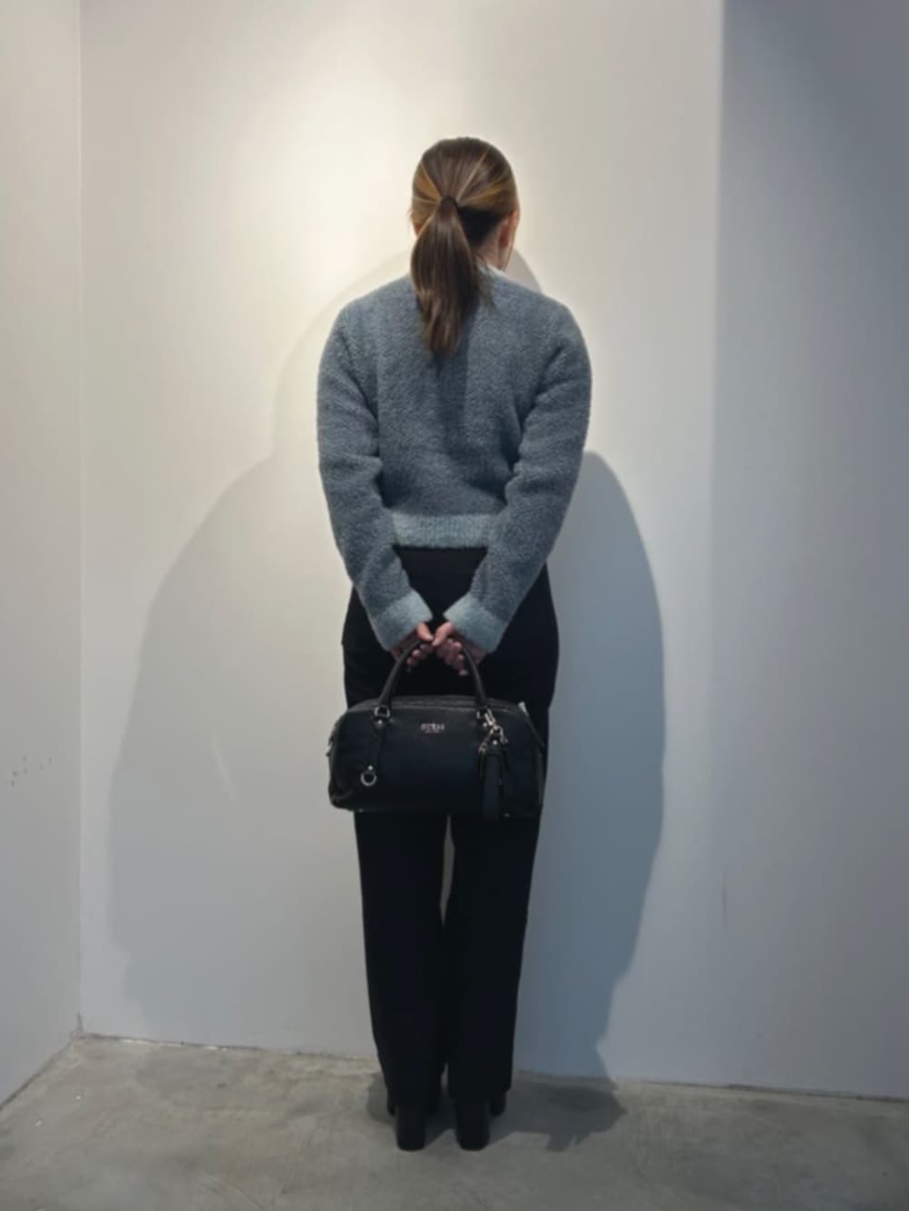 ブラック系のデニムパンツ、グレー系のニット/セーター、ブラック系のショルダーバッグを着用したレディースの冬コーディネートの2枚目の写真