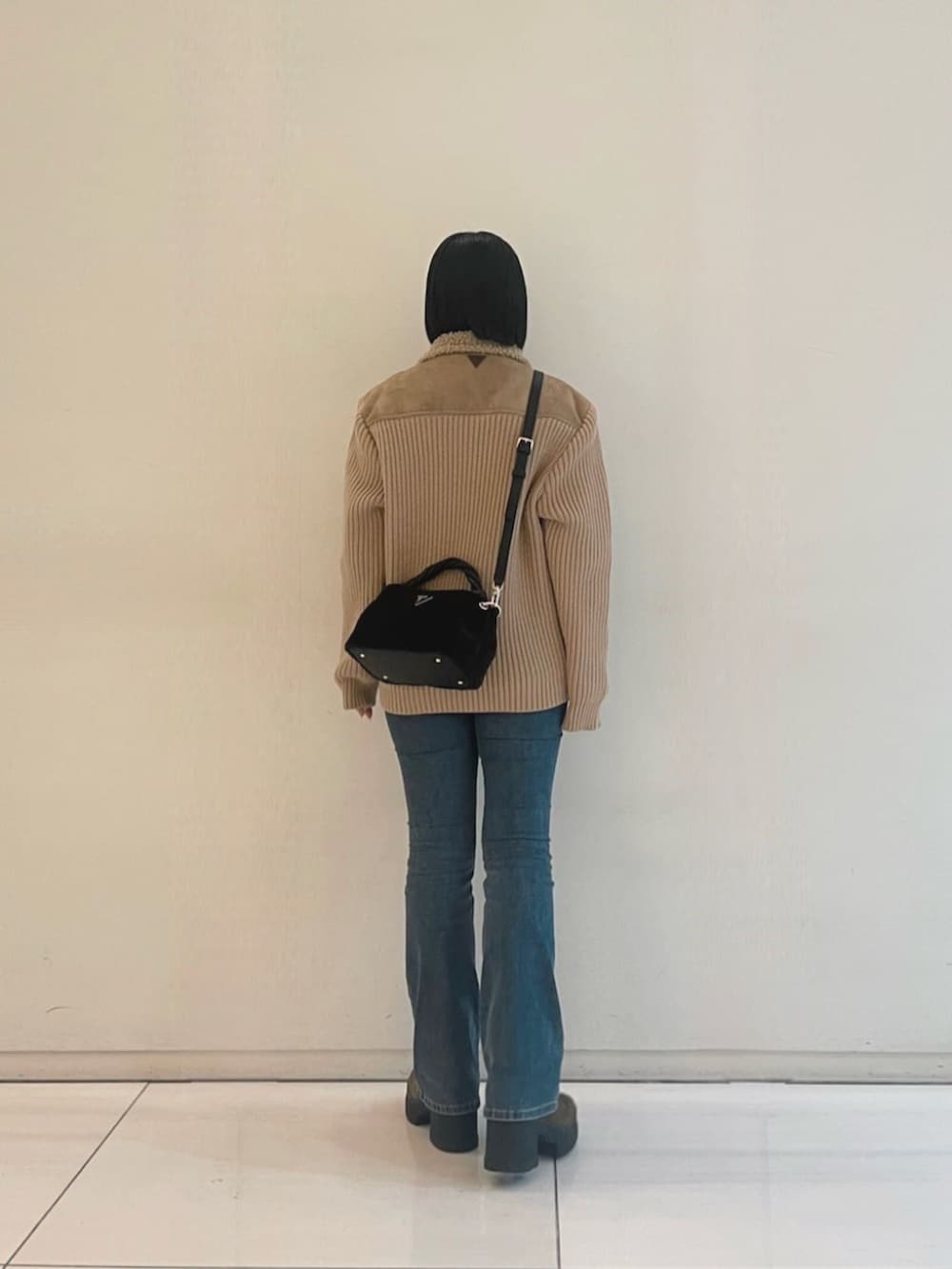 ブルー系のデニムパンツ、ブラック系のニット/セーター、ブラック系のショルダーバッグを着用したレディースの冬コーディネートの2枚目の写真