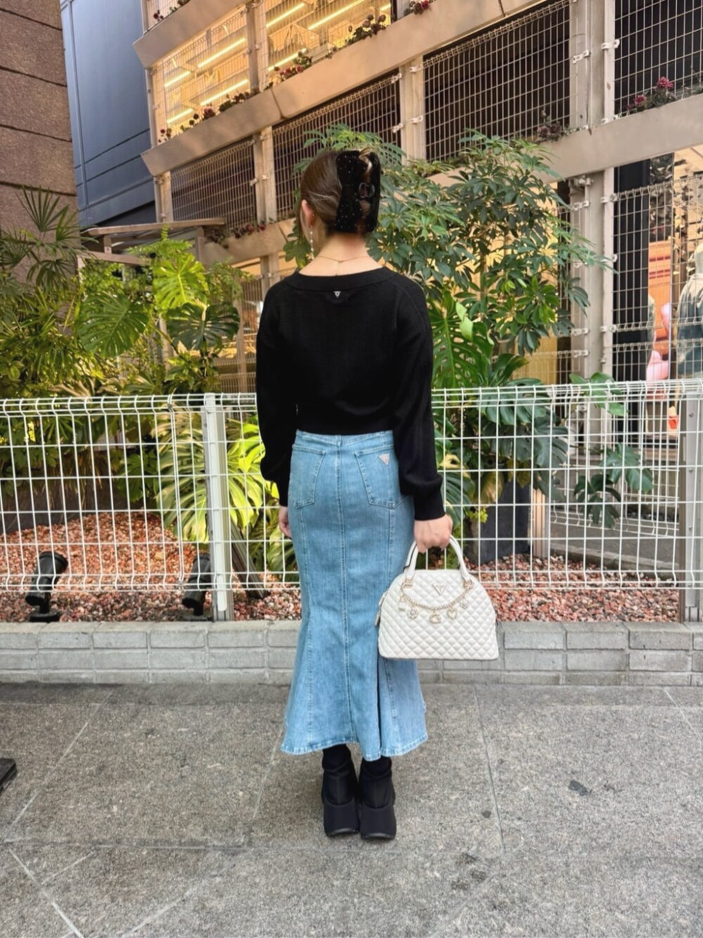 ブルー系のデニムスカート、ブラック系のカーディガン/ボレロ、ホワイト系のショルダーバッグを着用したレディースの秋コーディネートの2枚目の写真