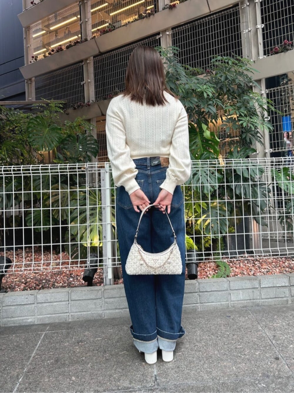 ブルー系のデニムパンツ、ホワイト系のハンドバッグ、ベージュ系のカーディガン/ボレロを着用したレディースの秋コーディネートの2枚目の写真