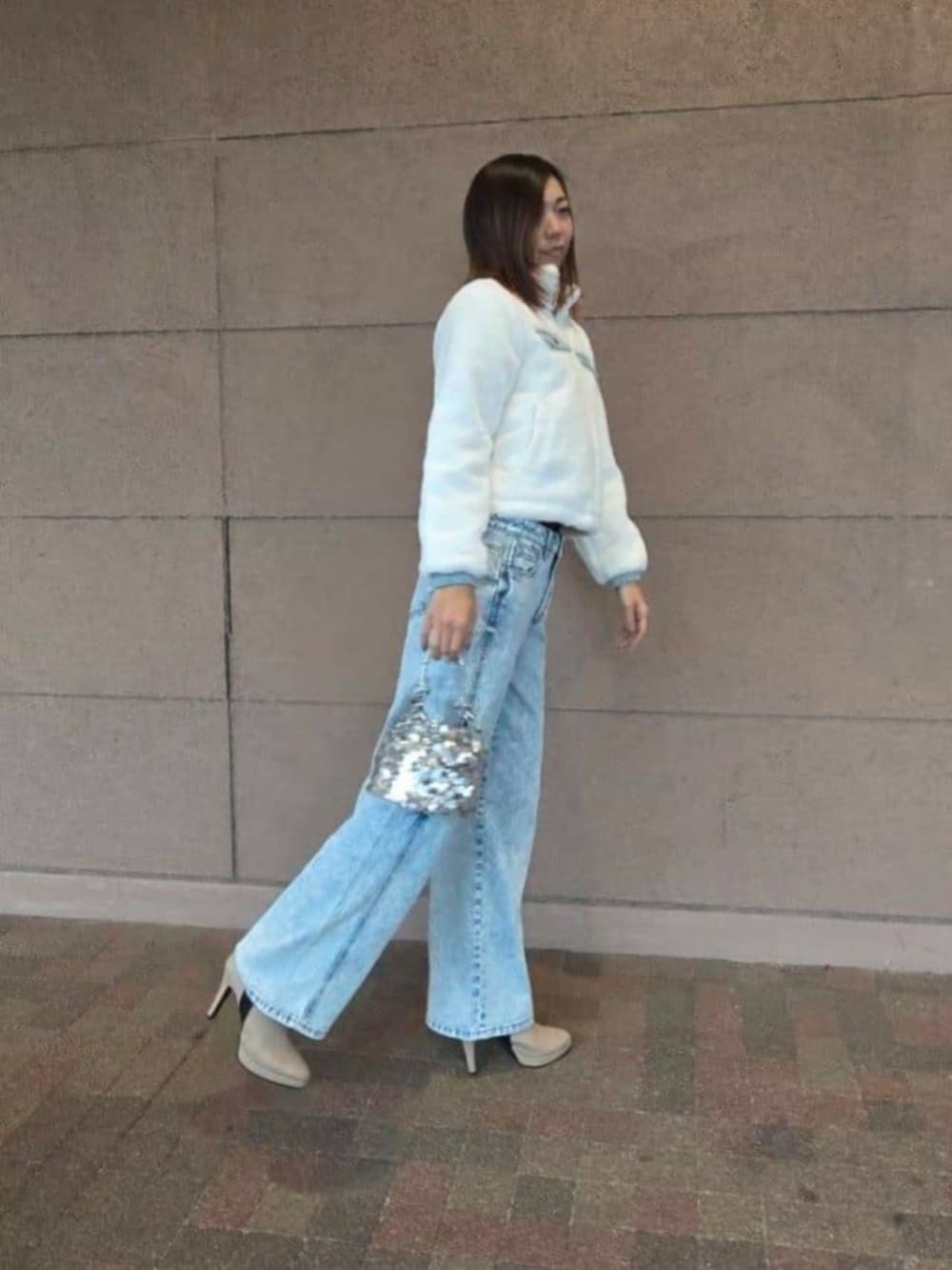 シルバー系のショルダーバッグ、ブルー系のデニムパンツ、ホワイト系のブルゾンを着用したレディースの冬コーディネートの3枚目の写真