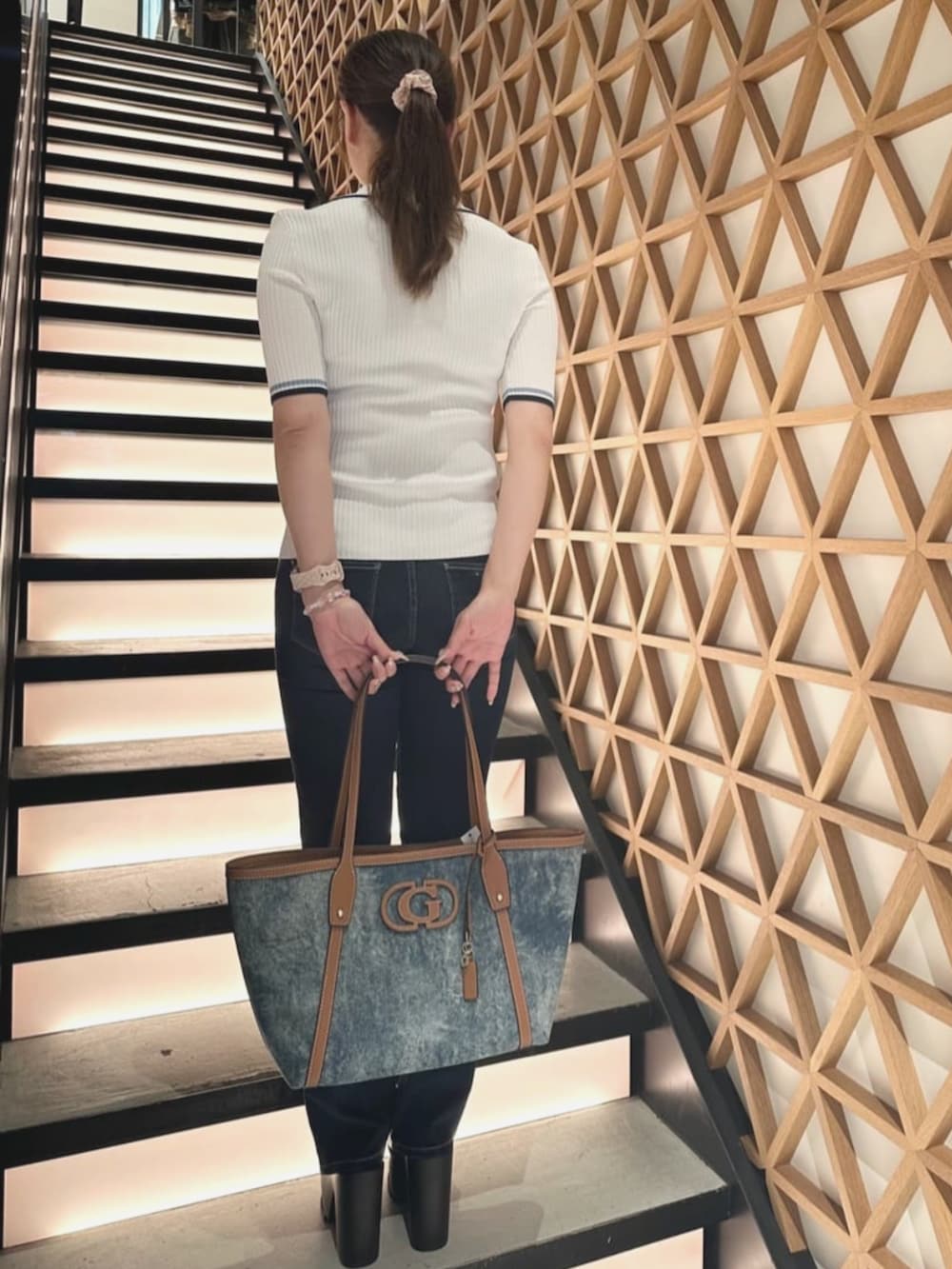 ブルー系のトートバッグ、ブルー系のデニムパンツ、ベージュ系のポロシャツを着用したレディースの夏コーディネートの2枚目の写真