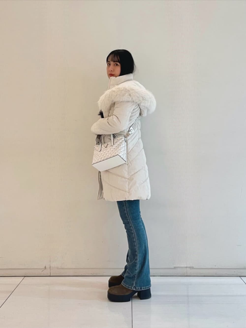 ブルー系のデニムパンツ、ブラック系のニット/セーター、ホワイト系のショルダーバッグを着用したレディースの秋コーディネートの3枚目の写真