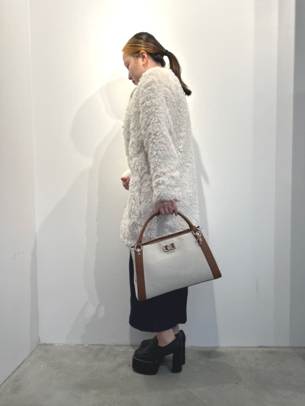 イエロー系のハンドバッグ、ホワイト系のカーディガン/ボレロ、ブルー系のワンピースを着用したレディースの冬コーディネートの3枚目の写真