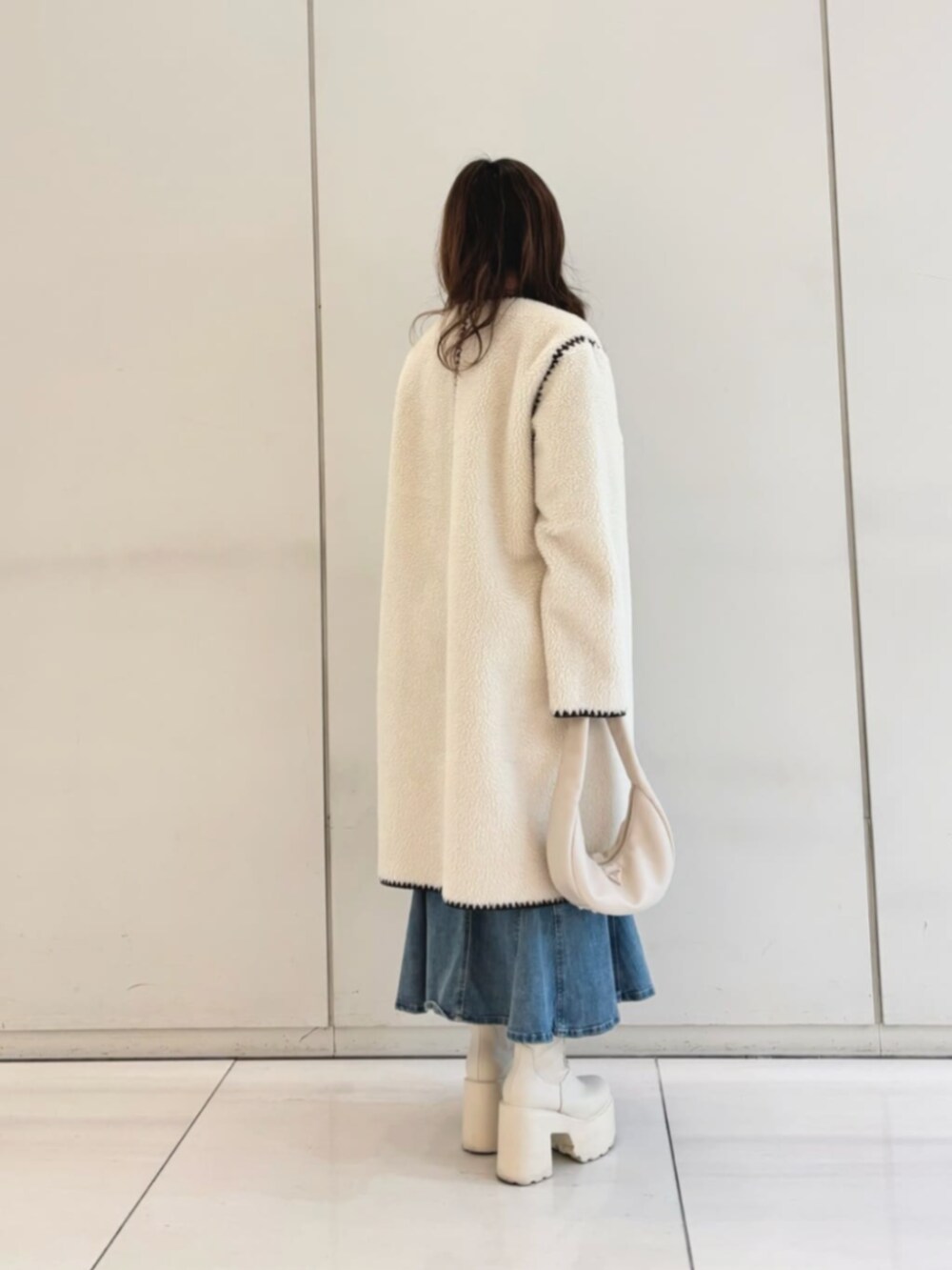 ブラック系のニット/セーター、ブルー系のデニムスカート、ホワイト系のショルダーバッグを着用したレディースの冬コーディネートの2枚目の写真