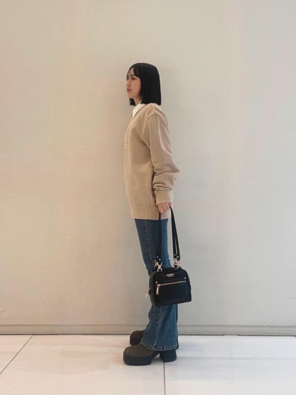 ブルー系のデニムパンツ、ベージュ系のポロシャツ、ブラック系のショルダーバッグを着用したレディースの冬コーディネートの3枚目の写真