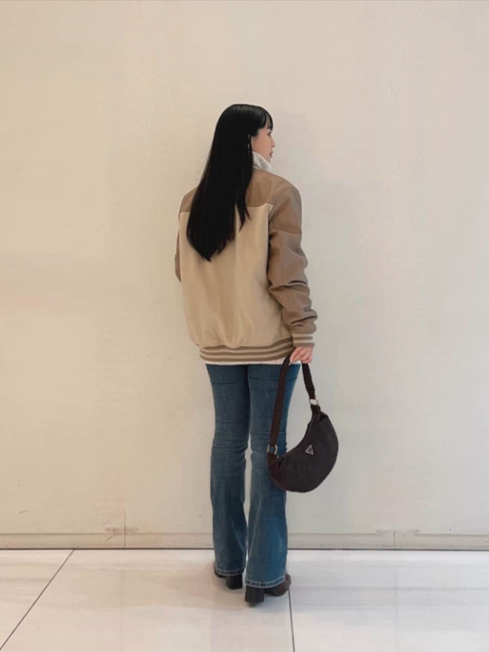 ブルー系のデニムパンツ、ブラウン系のショルダーバッグ、ベージュ系のスタジャンを着用したレディースの秋コーディネートの2枚目の写真