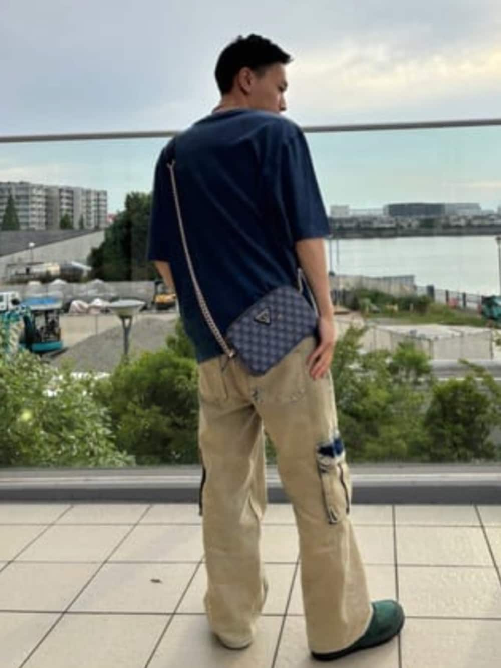 イエロー系のカーゴパンツ、ブルー系のショルダーバッグ、ブルー系のTシャツ/カットソーを着用したメンズの夏コーディネートの2枚目の写真