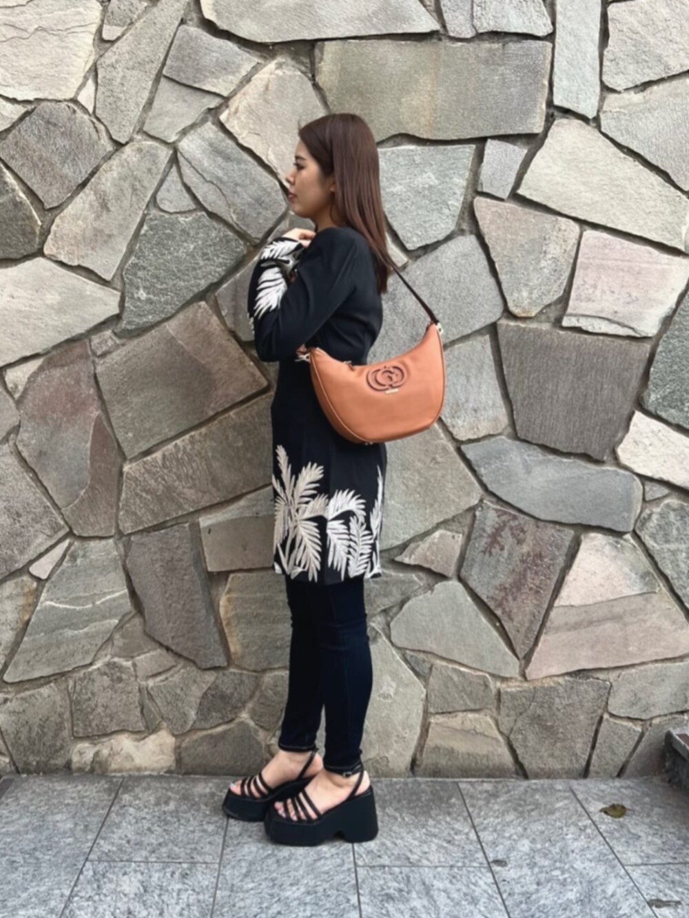 ブルー系のデニムパンツ、ブラック系のワンピース、ブラウン系のショルダーバッグを着用したレディースの秋コーディネートの3枚目の写真