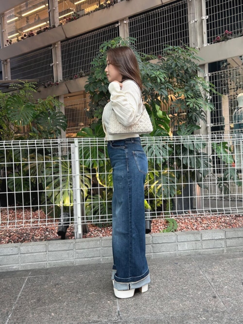 ブルー系のデニムパンツ、ホワイト系のハンドバッグ、ベージュ系のカーディガン/ボレロを着用したレディースの秋コーディネートの3枚目の写真