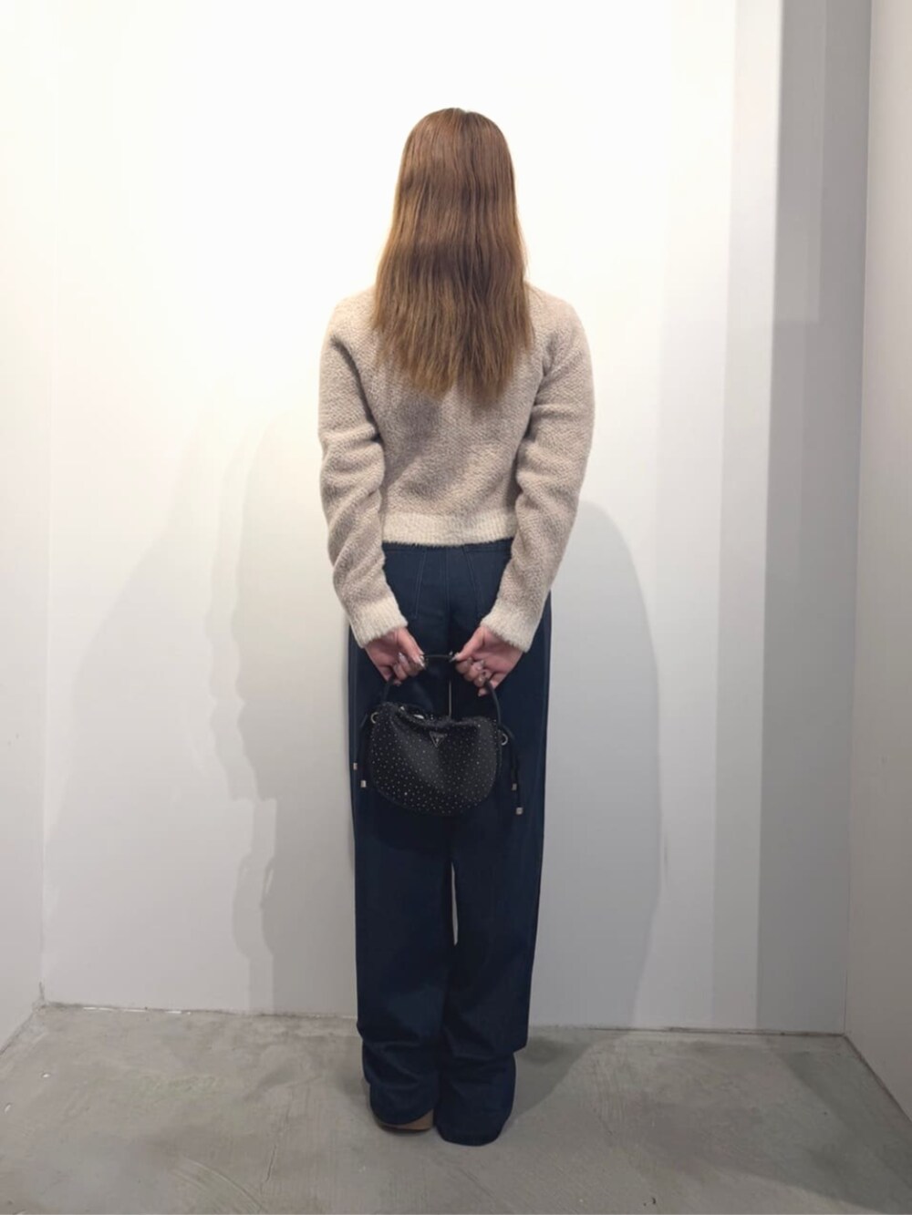 ブルー系のデニムパンツ、ベージュ系のニット/セーター、ブラック系のハンドバッグを着用したレディースの春コーディネートの2枚目の写真