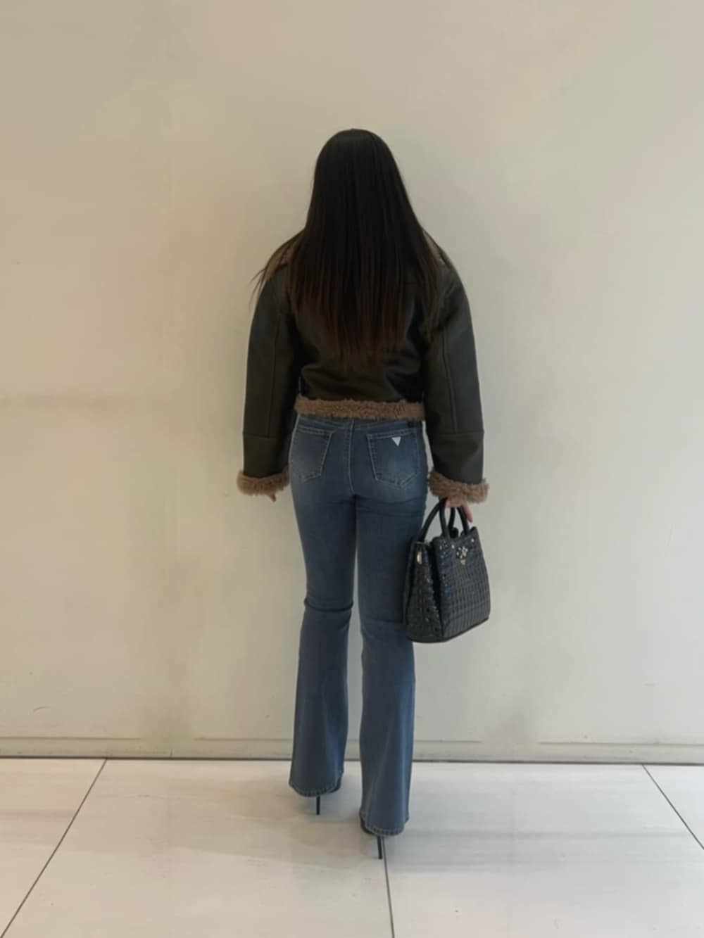 ブルー系のデニムパンツ、ブラック系のショルダーバッグ、ブラウン系のライダースジャケットを着用したレディースの冬コーディネートの2枚目の写真