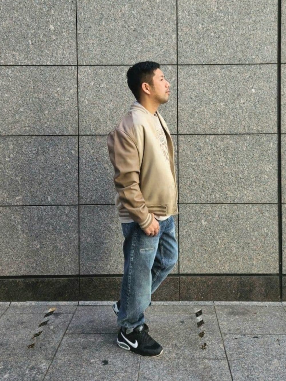 ブルー系のデニムパンツ、ベージュ系のスタジャン、ベージュ系のTシャツ/カットソーを着用したメンズの秋コーディネートの3枚目の写真