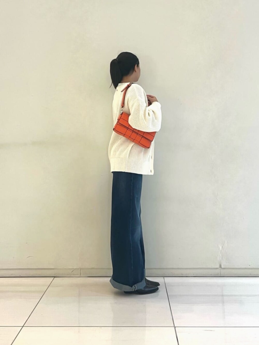 ブラック系のタンクトップ、ブルー系のデニムパンツ、オレンジ系のショルダーバッグを着用したレディースの秋コーディネートの3枚目の写真