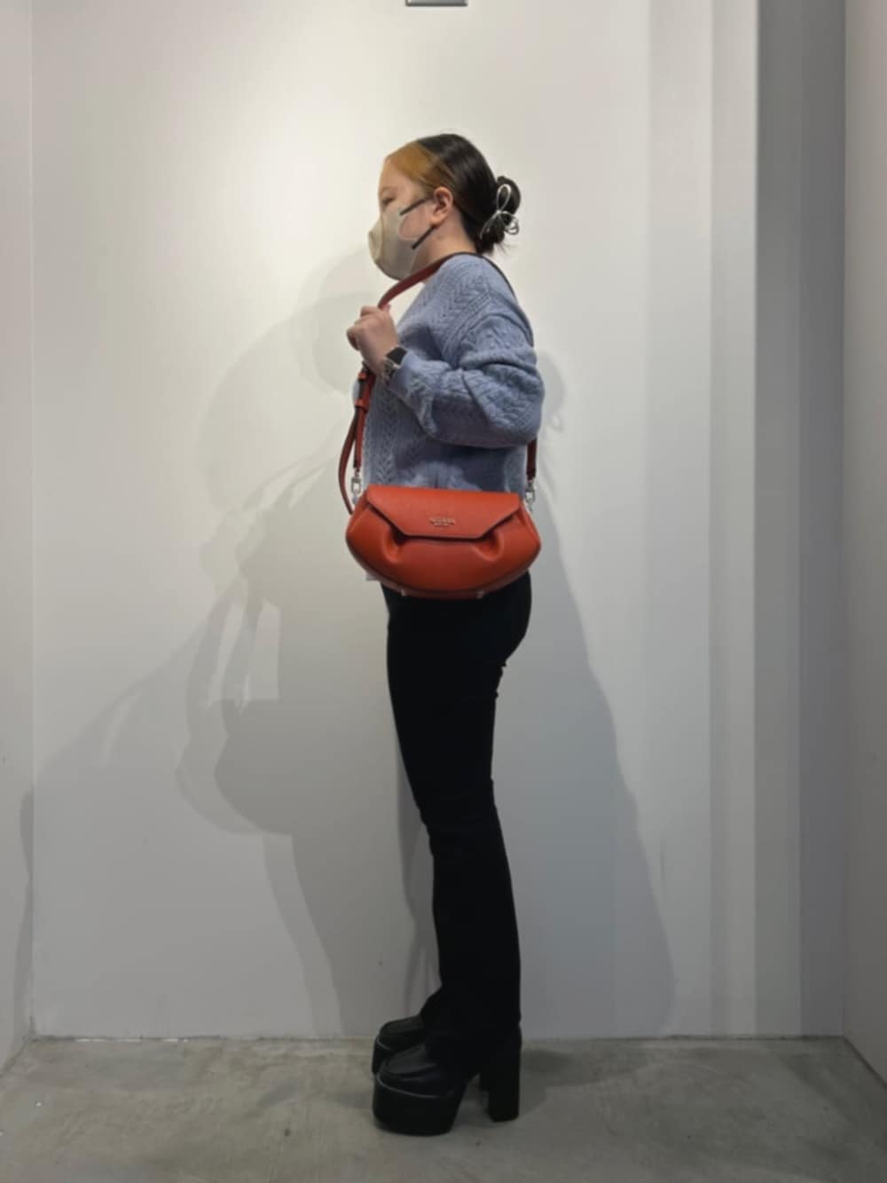 ブラック系のデニムパンツ、ブルー系のニット/セーター、オレンジ系のショルダーバッグを着用したレディースの冬コーディネートの3枚目の写真