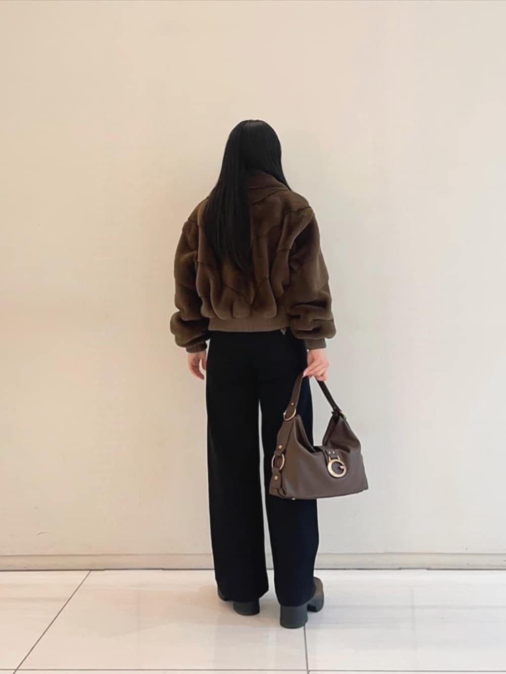 ブラック系のデニムパンツ、ブラウン系のショルダーバッグ、ブラック系のニット/セーターを着用したレディースの冬コーディネートの2枚目の写真