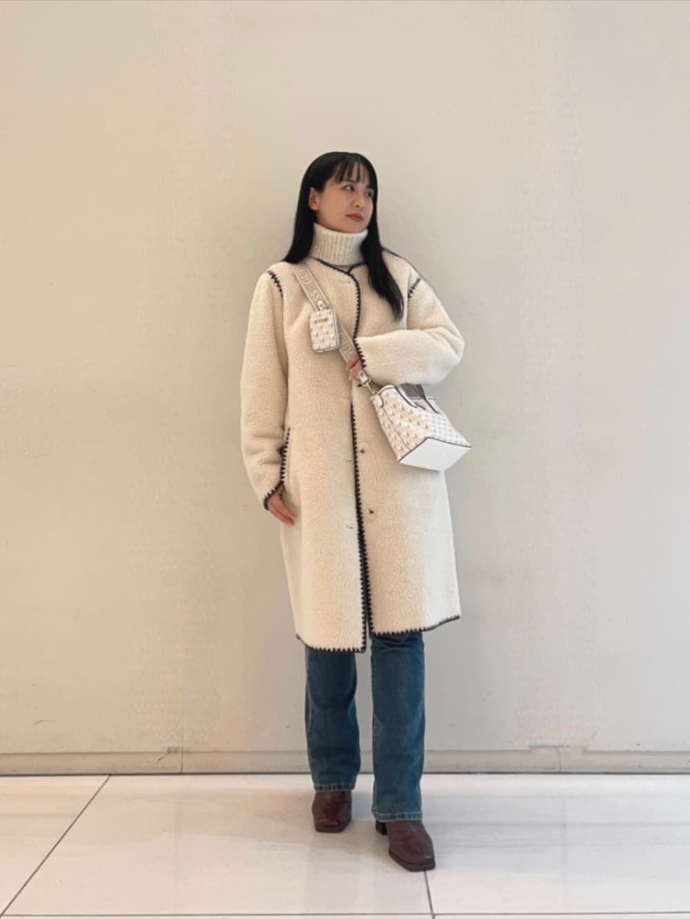 ブルー系のデニムパンツ、ホワイト系のショルダーバッグ、ベージュ系のニット/セーターを着用したレディースの秋コーディネートの4枚目の写真