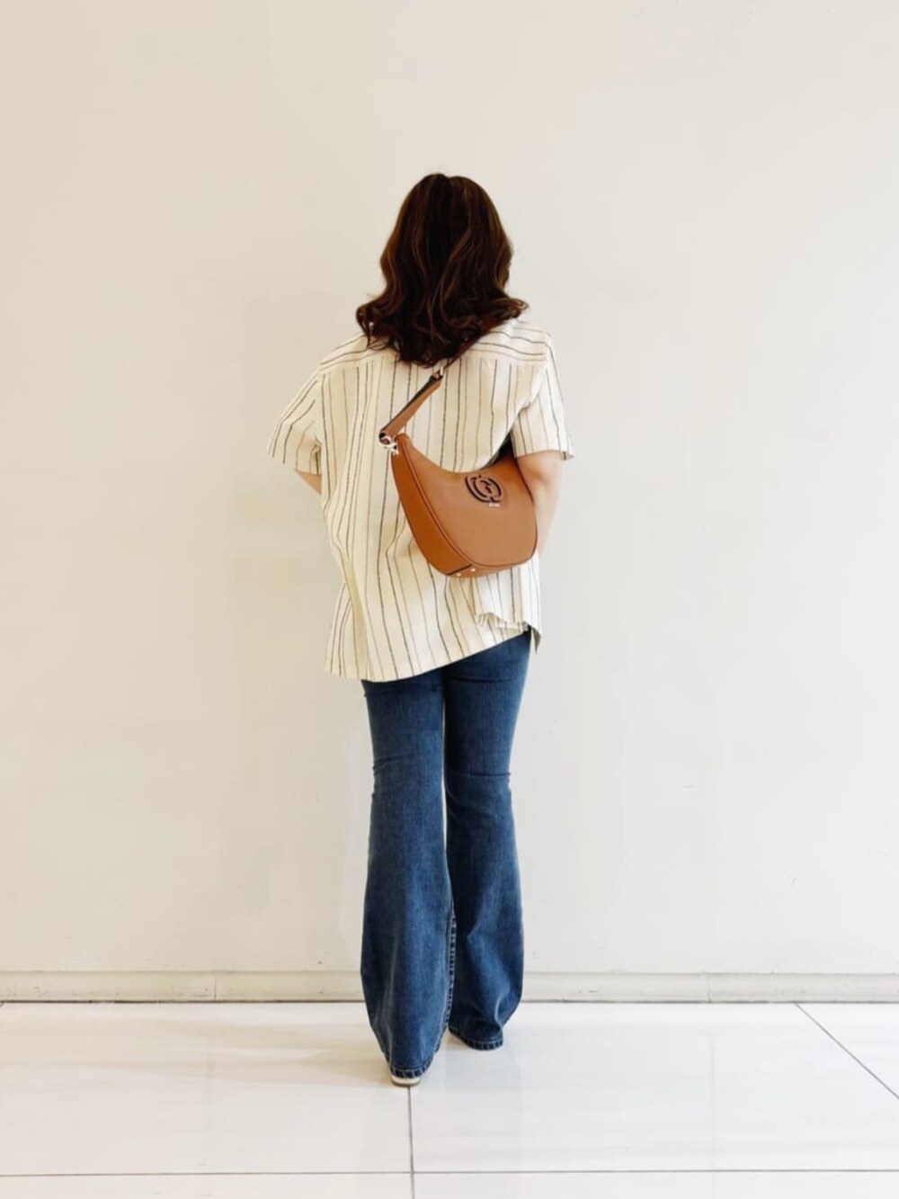 ブルー系のデニムパンツ、ホワイト系のシャツ/ブラウス、ブラウン系のショルダーバッグを着用したレディースの秋コーディネートの2枚目の写真