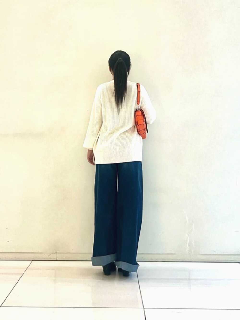 ブラック系のタンクトップ、ブルー系のデニムパンツ、オレンジ系のショルダーバッグを着用したレディースの秋コーディネートの2枚目の写真