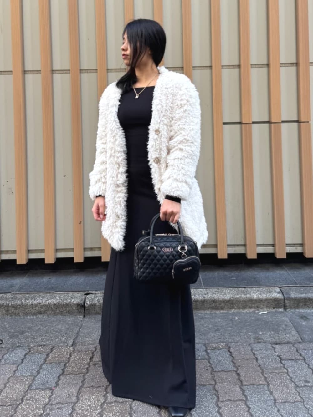 ブラック系のハンドバッグ、ブラック系のワンピース、ホワイト系のカーディガン/ボレロを着用したレディースの春コーディネートの3枚目の写真